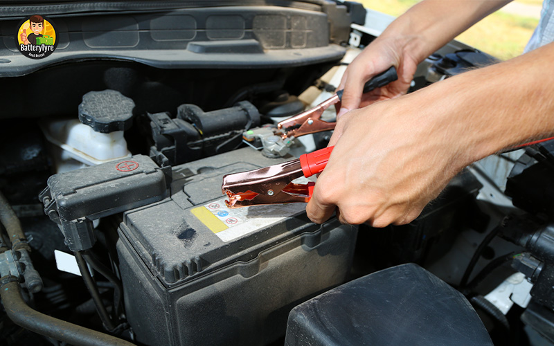 Driver attaching jumper cables to car battery terminals.