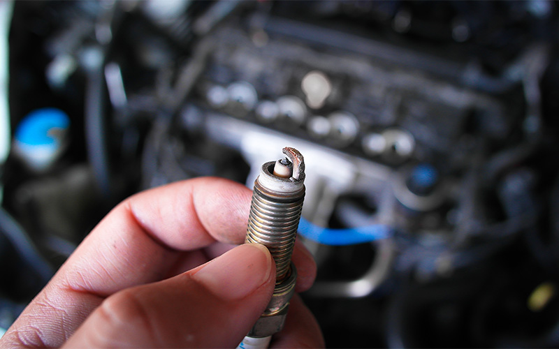 Hand holding a worn car spark plug.